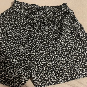 Svarta blommiga shorts från Amisu/ new yorker - Snygga svarta shorts från Amisu med ett vitt blommönster. Perfekta för en avslappnad sommarlook. De har en bekväm passform och elastisk midja för extra komfort.
