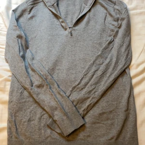 Grå halfzip Selected Homme - Säljer en stilren grå tröja från Selected Homme. Tröjan har en dragkedja vid halsen och är tillverkad i ett mjukt material. Perfekt för en avslappnad look. Använd enstaka gånger i riktigt fint skick!