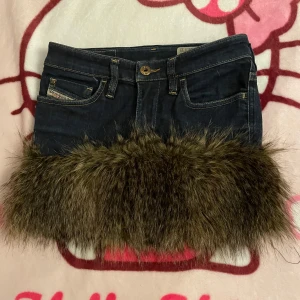 Mini tjol från diesel - Unik jeanskjol från Diesel med en cool pälsdetalj längst ner. Kjolen har klassiska femficksdesign och en mörk denimfärg. Perfekt om man söker sig en 2000-tals stil