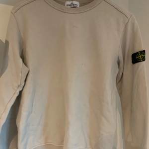 Beige Stone Island Junior Crewneck i storlek 156. Det finns lite småfläckar på tröjan. (se bild) De är dock inte så synliga. Tveka inte på att skriva om ni har några frågor!