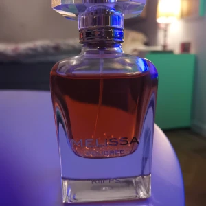 Melissa Eau de Parfum - Säljer en elegant parfymflaska från Riflessi med namnet Melissa. Flaskan är stilrent designad i glas med en vacker, djup bärnstensfärgad vätska. Korken är facetterad och ger en lyxig känsla. Perfekt för den som vill ha en sofistikerad doftupplevelse. 85 % kvar 