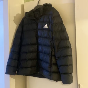 Svart jacka från Adidas - Säljer en svart dunjacka från Adidas i mycket bra skick. Jackan har en dragkedja framtill och en mysig huva. Jackan har två fickor.