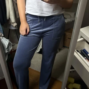 Blå mjukisbyxor från Juicy Couture - Säljer ett par superbekväma blå mjukisbyxor från Juicy Couture. De har en loose passform och är perfekta för en chill dag hemma. Byxorna har fickor med knappar bak och en snygg detalj med loggan på sidan. Perfekta för höst och vinter! Storlek 170 barn!