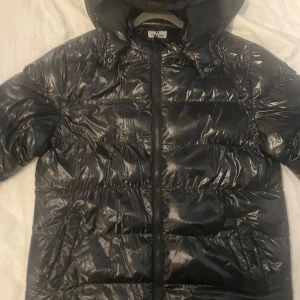Svart  pufferjacka med huva - Säljer en svart  pufferjacka i herrstorlek M. Jackan har en praktisk huva och stängs med dragkedja. Perfekt för kyliga dagar och ger en stilren look. Använd ett fåtal gånger, så den är i mycket bra skick. Passar perfekt för höst och vinter!