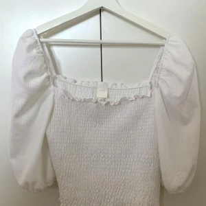 Smockad blus med puffärm - Endast använd vid några få tillfällen och är således i mycket fint skick! Normal i storleken och därtill stretchig i och med det smockade tyget. Croppad modell!