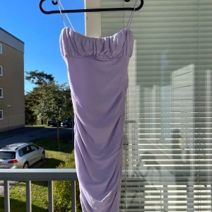 Ljuslila klänning med rynkdetaljer - Säljer en helt ny superfin ljuslila klänning med smala axelband och rynkdetaljer som ger en snygg passform. Perfekt för sommarens fester eller en utekväll. Klänningen är axelbandslös och har en elegant, figurnära design. Från princess polly.