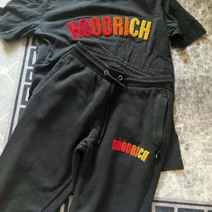 Svart t-shirt från Hoodrich - Säljer en svart t-shirt från Hoodrich med färgglatt broderat märke på bröstet. Perfekt för en avslappnad stil och passar bra till vardags eller chillhäng. T-shirten har en normal passform och är gjord i mjukt material för extra komfort.
