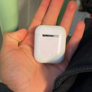 Trådlösa hörlurar med laddningsetui - Säljer ett par trådlösa hörlurar i ett vitt laddningsetui. Etuiet har en smidig design och en laddningsport på undersidan. Hörlurarna är bekväma och passar perfekt för musik och samtal på språng.