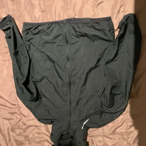 Svart vindjacka från SOC - Säljer en svart vindjacka från SOC. Den är perfekt för blåsiga dagar med sitt vindtäta material. Jackan har en dragkedja framtill och är långärmad. Den är i bra skick och passar perfekt för utomhusaktiviteter.