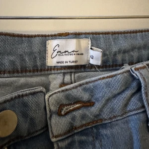 Blå jeans från Emma Ellingsen - Säljer ett par snygga blå jeans från NA-KD x Emma Ellingsen. De är i storlek 42 och har en klassisk design med knappar och dragkedja. Jeansen har en rak passform och är perfekta för både vardag och fest. 