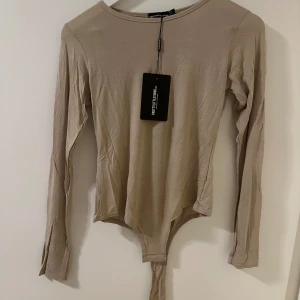 Beige långärmad topp från PrettyLittleThing - Säljer en snygg beige långärmad topp/body från PrettyLittleThing. Den är perfekt för både vardag och fest med sin stilrena design. Toppen är i ett mjukt och bekvämt material och har en tight passform.
