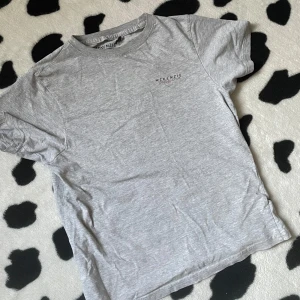 Grå t-shirt från McKenzie - Säljer en stilren grå t-shirt från McKenzie. Den har en enkel design med korta ärmar och en liten logga på bröstet. Perfekt för en avslappnad look.