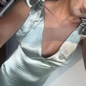 Ljusgrön långklänning från Pretty Lavish - Elegant ljusgrön långklänning från Pretty Lavish i satin. Klänningen har en v-ringad design med knytbara axelband och en smickrande passform. Den är maxi lång och perfekt för balen!!