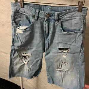 Jeansshorts med slitningar - Säljer ett par ljusa jeansshorts med slitningar och fransiga kanter. Perfekta för en avslappnad stil. De har en klassisk femficksdesign.