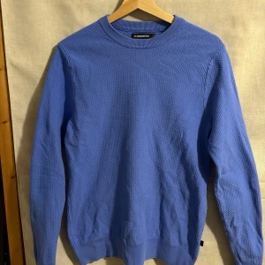 Blå tröja från J.Lindeberg - Snygg blå tröja från J.Lindeberg med ett diskret texturerat mönster. Tröjan har långa ärmar och en rund halsringning. Perfekt för en stilren look.