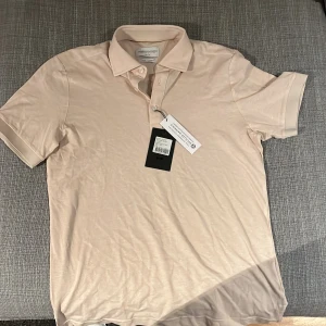 Beige kortärmad pikétröja från j.Harvest&frost  - Snygg beige pikétröja från j.Harvest&frost med klassisk krage och knappar framtill. Perfekt för en stilren look. Passar bra till både jeans och chinos.