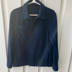 Mörkblå overshirt från donce de la sense  - Säljer en stilren mörkblå overshirt med knappar framtill. Jackan har två bröstfickor och långa ärmar, perfekt för en avslappnad look. Passar bra nu till våren. Ifall du har några funderingar är de bara att höra av dig MVH/William 
