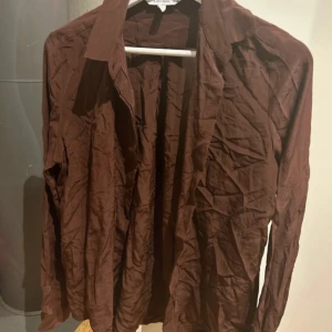 Brun siden skjorta från Other Stories stl 34 - Säljer en brun skjorta från Other Stories. Skjortan har långa ärmar och en klassisk krage. Perfekt för en stilren look. 100% Siden/silke stl 34