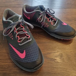 Nike FS Lite Run NYA - Helt nya snygga grå Nike löparskor med rosa detaljer och snörning. Skorna har en mönstrad sula för bra grepp och en sportig design. Perfekta för träning eller en aktiv vardag. US 7, UK 4,5 EUR 38. NIKEARTNR: 684667-005