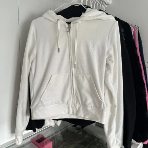 Vit hoodie från Juicy Couture - Säljer en stilren vit hoodie från Juicy Couture med dragkedja och huva. Tröjan har långa ärmar och praktiska fickor framtill. Perfekt för en avslappnad look.