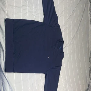 Mörkblå tröja från GANT - Säljer en stilren mörkblå tröja från GANT i storlek XL. Tröjan har långa ärmar och en liten logga på bröstet. Perfekt för en avslappnad och snygg look. 