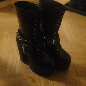 Svarta platåboots med nitar och kedja - Snygga svarta platåboots med hög klack och snörning. Skorna har coola detaljer som nitar och en kedja runt ankeln. Perfekta för att ge din outfit en edgy touch.