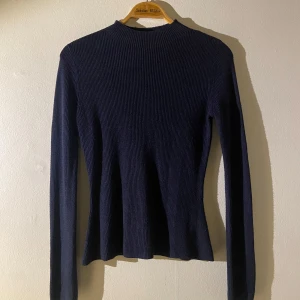 Mörkblå ribbad tröja - Stickad mörkblå tröja med extra långa armar. Den är något figursydd.