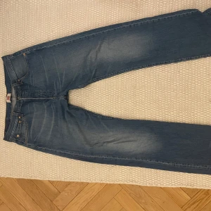 Blå jeans från Levi's - Snygga blå jeans från Levi's med klassisk femficksdesign och knappgylf. De har en rak passform och är perfekta för en avslappnad stil. Levi's-loggan syns på bakfickan och bältesskylten.
