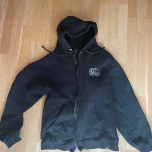 Svart hoodie från Spitfire - Säljer en svart hoodie från Spitfire med dragkedja och huva. Den har ett tryck med Spitfire-loggan på bröstet och små röda detaljer. Storlek M men sitter som S. Perfekt för en avslappnad stil.