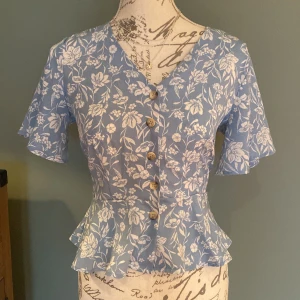 En blå tröja med vita blommor och knappar - Bra för sommaren och passar väldigt bra med jeans 