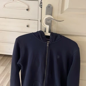 Mörkblå hoodie från U.S. Polo Assn. - Säljer en stilren mörkblå hoodie från U.S. Polo Assn. med dragkedja och huva. Perfekt för en avslappnad look. Den har långa ärmar och en praktisk ficka framtill. Väldigt bra passform måste jag säga och riktigt snygg 🤩 