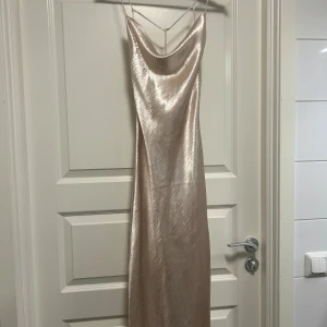 Champagnefärgad långklänning från Gina tricot  - Elegant champagnefärgad långklänning från Gina Tricot i glansigt/sidenaktigt material. Aldrig använd, lapparna är kvar. Köpt från Gina för 500kr. 