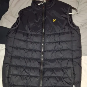 Svart lyle&scott dunväst - Västen passar barn runt 14-15års åldern.Den har ett litet håll i nedre kant som du kan se på första bilden.(pris kam diskuteras)