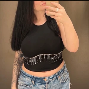 Svart ärmlös topp med pärldetaljer - Snygg svart ärmlös topp med pärldetaljer längs nederkanten. Perfekt för en stilren och trendig look. Passar bra till jeans eller kjol för en chic outfit.