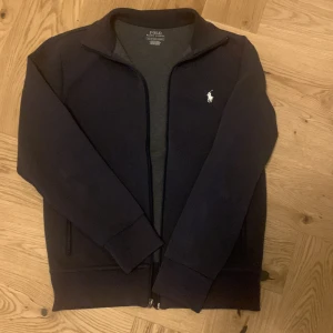 Mörkblå tröja från Ralph Lauren - Säljer en stilren mörkblå tröja från Ralph Lauren med dragkedja och det klassiska broderade logotypen på bröstet. Tröjan har långa ärmar och en bekväm passform. Perfekt för en avslappnad look. Sitter bäst på dig som är mellan 160 - 172