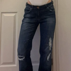 Lågmidjade bootcut jeans - Snygga mörkblå jeans med slitningar på benen. De har en klassisk femficksdesign och knappgylf. Perfekta för en avslappnad stil.