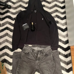 Svart hoodie från Polo Ralph Lauren - Säljer en stilren svart hoodie från Polo Ralph Lauren med dragkedja och det klassiska logotypen på bröstet. Perfekt för en avslappnad look. Den har långa ärmar och en praktisk huva med dragsko. Storlek S