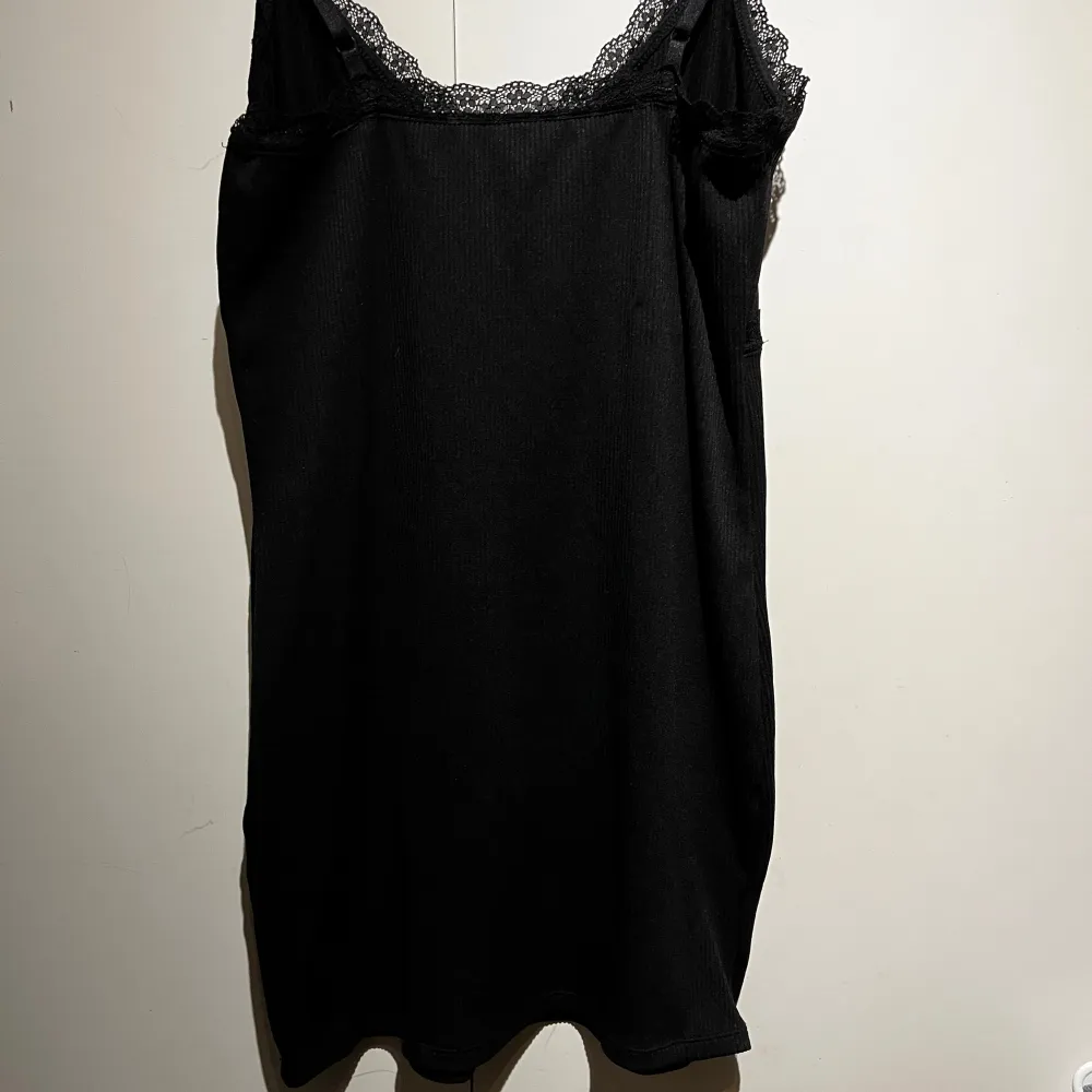 Elegant svart klänning med spetsdetaljer vid halsringningen och axelbanden. Perfekt för en stilren look. Klänningen har en enkel och klassisk design som passar många tillfällen.. Mekot.