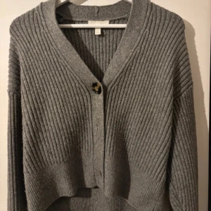 Grå ribbad kofta från H&M - Säljer en stilren grå ribbad kofta från H&M. Koftan har en knapp framtill och är perfekt för kyligare dagar. Den har en klassisk design med långa ärmar och en bekväm passform.