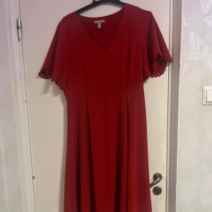Röd klänning från H&M - Snygg röd klänning från H&M med v-ringning och kortärmade ärmar med fina detaljer. Perfekt för en elegant look. Klänningen har en klassisk design som passar många tillfällen.