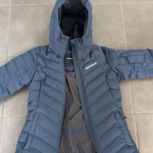 Mörkblå dunjacka från Peak Performance - Säljer en snygg mörkblå dunjacka från Peak Performance. Jackan har en praktisk huva och dragkedja framtill. Perfekt för våren, sen vinter och höst.  .