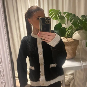 Svart och vit kofta från Holly & Whyte - Säljer en snygg svart kofta med vita detaljer från Holly & Whyte. Koftan har knappar framtill och två fickor. Perfekt för att hålla sig varm och stilren. Passar till många olika outfits!