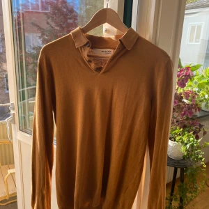 Brun tröja från Selected Homme - Snygg brun tröja från Selected Homme med krage och knappar. Perfekt för en stilren look. Tröjan har långa ärmar och är tillverkad i ett mjukt material. Finns ett mycket litet hål i sömnen på baksidan, men det syns knappt vid användning.