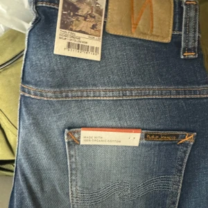 Blå jeans från Nudie Jeans w28 L /32 - Snygga blå jeans från Nudie Jeans i en klassisk straight passform. Tillverkade av 100% ekologisk bomull med en stilren design och subtila slitningar för en trendig look. Perfekta för en avslappnad stil.