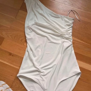 Vit asymmetrisk body - Snygg vit body med en axel och rynkdetaljer på sidan.