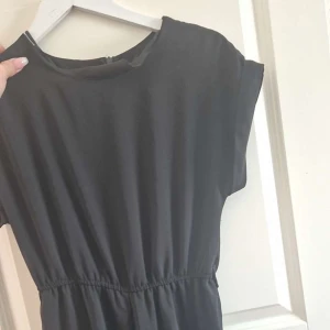 Svart klänning med resår i midjan - Säljer en stilren svart klänning med resår i midjan. Klänningen har korta ärmar och en enkel design som passar perfekt för olika tillfällen. Den är gjord i ett mjukt och bekvämt material.