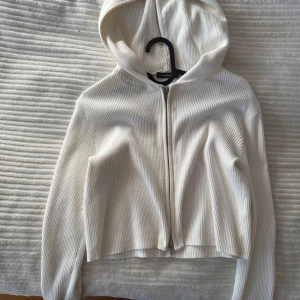 Vit ribbad hoodie från Brandy Melville - Säljer en stilren vit ribbad hoodie från Brandy Melville. Den har en dragkedja framtill och en mysig huva. Perfekt för en avslappnad look.