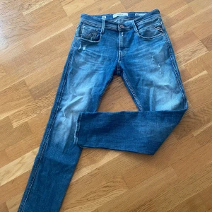 Blå jeans från Replay - Snygga blå jeans från Replay, modell Anbass. De har en klassisk femficksdesign med dragkedja och knapp. Jeansen har en lätt slitning för en cool look.