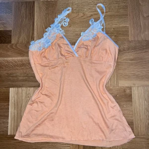 Orange topp från vila - Säljer en söt orange linnetopp från Vila med vackra spetsdetaljer i vitt vid axelbanden. Toppen har en v-ringad design och är perfekt för varma dagar. Den är tillverkad i ett mjukt och bekvämt material. Färgen stämmer mest in på sista bilden, dåligt ljus på de första två