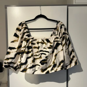 Mönstrad topp - Säljer en trendig offshoulder topp med ett djärvt mönster i svart och beige. Toppen har vida trekvartsärmar och en lös passform.